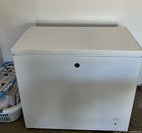 Front view of white GE chest freezer with small discoloration on bottom corner and visible keyhole lock on front.