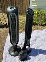 Two Honeywell tower fans and one small Kaz Everstar heater shown on outdoor sheet. One fan missing plastic on top, all items powered with visible controls.