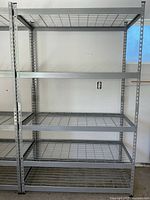 Photo of a large, adjustable steel rack with five wire mesh shelves against a white wall.