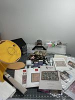 Full view of the needlework stand with embroidery hoop, clip-on lamp, thread spools, measuring mats, and pattern packets spread on the table.