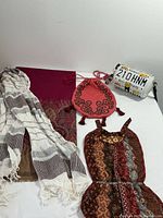 Photo showing white and brown striped scarf, fuchsia patterned wrap, coral drawstring pouch, sequined bag, and Hawaii metal license plate clutch