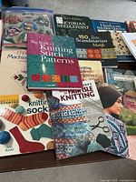 Photo showing a collection of knitting and quilting pattern books arranged on a table, featuring colorful book covers focused on knitting socks, sweaters, and quilting.