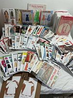 Photo showing wide assortment of sewing patterns arranged in fan shape with packages showing multiple types of women's clothing including aprons, dresses, shirts, skirts, and pants.