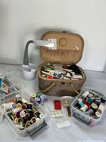 Photo of entire sewing basket with sewing tools, three plastic boxes filled with sewing thread spools in assorted colors, and OttLite desk lamp.
