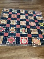Full view of one quilt laid flat on floor showing checkerboard patchwork design and patterned edge