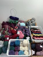 Photo showing mixed yarn skeins including purples, blues, pinks, and reds with partially finished projects and circular needles.