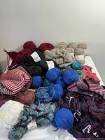 Various balls of yarn in colors including red, black, blue, beige, white, multicolor, and striped patterns with partially finished knitting projects