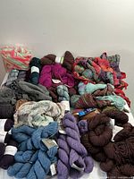 Photo showing multiple skeins of yarn in colors including blue, purple, grey, brown, and multicolor along with partially knitted projects.