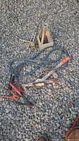 Group view of camper jack stand, jumper cables, cable puller, lug wrench on gravel