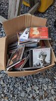 Open cardboard box containing stack of CD jewel cases, visible titles