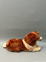 Side view of the 1950s Lassie plush dog showing brown and white plush fabric and rubber nose lying on flat surface.