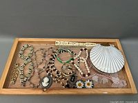 Photo of assorted costume jewelry in wooden tray showing various necklaces, bracelets, hand fan case, cameo brooch, and vanity box.