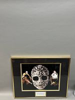 Full view of the framed photo showing three images (large mask close-up center, two smaller action shots of Gerry Cheevers in Boston Bruins uniform on either side) and bottom plaque.
