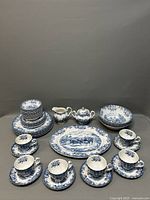 Full set displayed including cups with saucers, plates, bowls, creamer, sugar bowl and platter, all blue and white with coaching scene design.