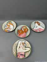 Four Le Belle Femme collector plates arranged on a gray surface showing various women with floral and flowing hair designs.
