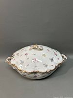 Covered porcelain tureen with floral designs and gold trim, with lid on showing handle and decorative edges.