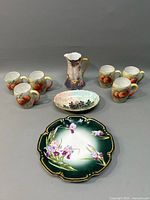 Full set with five peach-decorated cups, purple floral pitcher, oval dish, and green floral plate