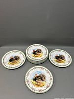 Nine dinner plates arranged with some stacked and others spread out, showing the turkey motif and floral border on white porcelain.