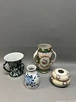 Four Asian porcelain items shown: a black and white floral vase, white and blue small vase, large decorated vase with handles, and round floral hair receiver dish.