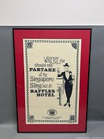 Close-up photo of the framed advertising print on linen with black typography and illustrated man promoting Singapore Sling at Raffles Hotel.
