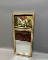 Full view of the split mirror with floral painting on top and mirror below in a gold-tone carved frame.
