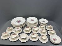 Overall view of the Wedgwood Wellesley china set showing various plates, cups and saucers with floral pattern and embossed border detail.