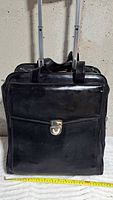 Front view of black leather rolling bag showing telescopic handle, clasped flap pocket and overall condition