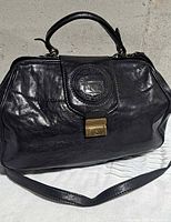 Front of black leather Pettinati Boston bag showing logo medallion and turn-lock clasp
