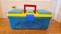 Photo showing the front view of the blue storage box with yellow lid and red handle; beads visible inside