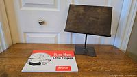 Cast iron music/book stand displayed on wooden table alongside piano music primer book