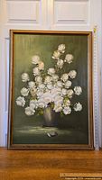 Full front view of the signed oil painting showing the bouquet of white roses in a gray vase against a green background.
