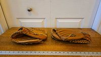 Two tan adult sized baseball gloves laid side by side showing size comparison and condition.