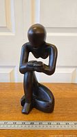 Front view of the wooden thinker sculpture showing the figure seated with head bowed and arms resting on knees.
