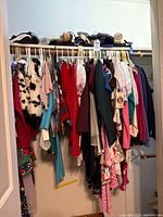 Full closet view of hanging children’s clothing and shoes on upper shelf