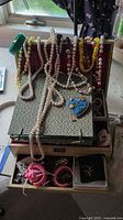 Overall view of open jewelry box with necklaces draped, heart pendant and compartments visible