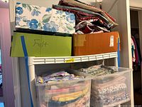 shelf holding two cardboard boxes and two clear bins filled with folded fabric