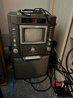 Front view of karaoke machine showing CD player section, CRT screen, cassette deck and attached microphone