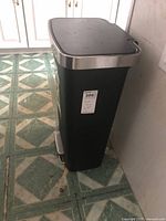 Full view of black rectangular trash can, lid closed, foot pedal visible