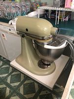 Front left view of green KitchenAid stand mixer with stainless steel bowl attached, on countertop
