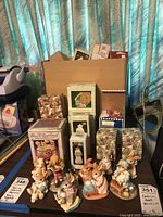 Overall view of boxed Precious Moments items, unboxed bunny figurines and cardboard box of extras