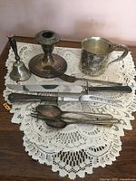 Entire lot on lace doily showing candlestick, bell, cup and utensils