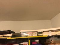 Top shelf with folded linens stack and plastic bin containing packaged linens