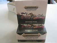 Photo of two sealed boxes of Warhammer Age of Sigmar Champions booster packs showing front of boxes with fantasy battle artwork and branding.