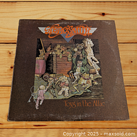 Front cover of Aerosmith Toys in the Attic album showing detailed illustrated artwork of toys and creatures around a fireplace with title and band logo.