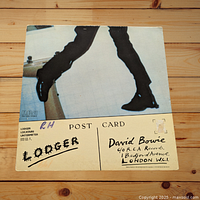 Backside of David Bowie postcard showing 'Lodger' text and RCA Records address, with handwritten marks and a small price tag.