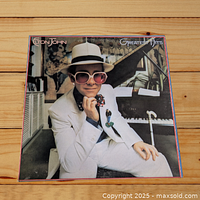 Front cover of Elton John Greatest Hits LP, showing Elton John in white suit and hat with piano background.