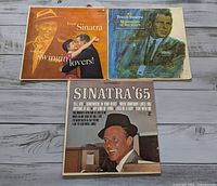 Three Frank Sinatra vinyl LP albums displayed on a wooden surface: Sinatra '65, Songs for Swingin' Lovers, and September of My Years.