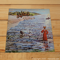 Front cover of Genesis Foxtrot vinyl album showing illustrated seaside scene with fox-headed figure and 'Genesis Foxtrot' title.