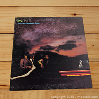 Front cover of Genesis LP album titled "And Then There Were Three..." showing three men and a car at sunset with dark clouds.