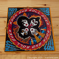 Front cover of the KISS Rock and Roll Over LP, showing colorful illustrated artwork of the band members' faces in circle with flames and electric lightning, text in red and blue.